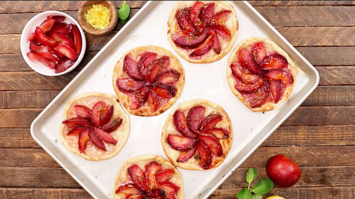 overhead shot of 6 baked plum tarts on a half-sheet pan