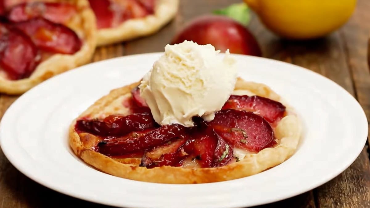 horizontal view showing how to serve a baked plum tart topped with a scoop of ice cream