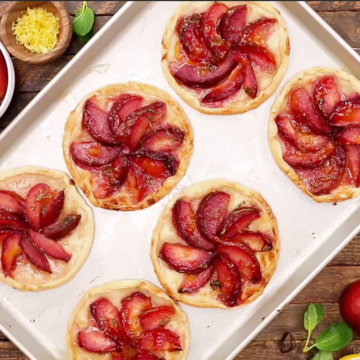 overhead shot of 6 baked plum tarts on a half-sheet pan