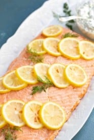 Poached salmon garnished with lemon slice and dill, with a side of cucumber dill sauce