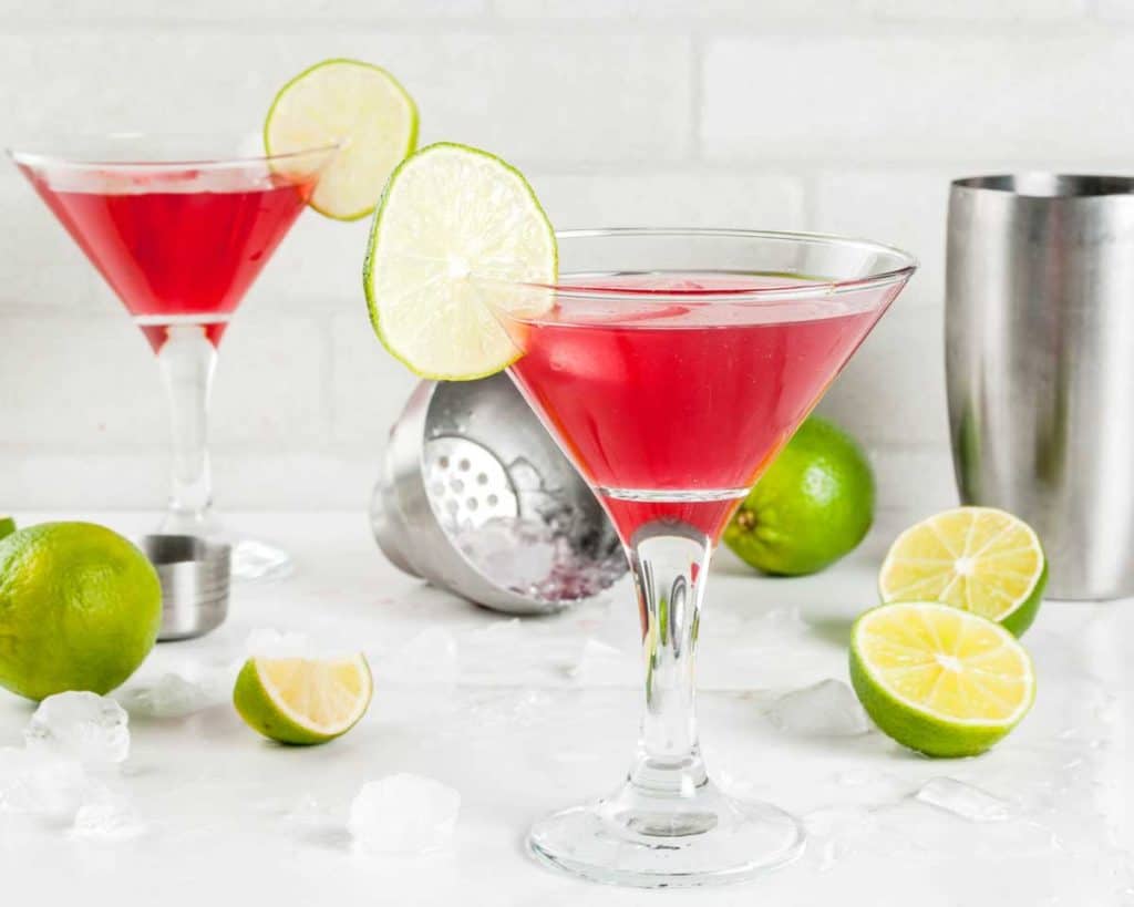 shot of two prepared Pomegranate Martinis with limes and a shaker