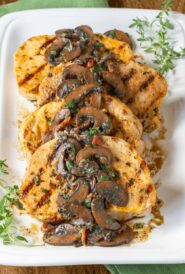 Four pork chops on a white latter with mushroom sauce spooned over top, garnished with fresh thyme