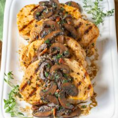 Four pork chops on a white latter with mushroom sauce spooned over top, garnished with fresh thyme