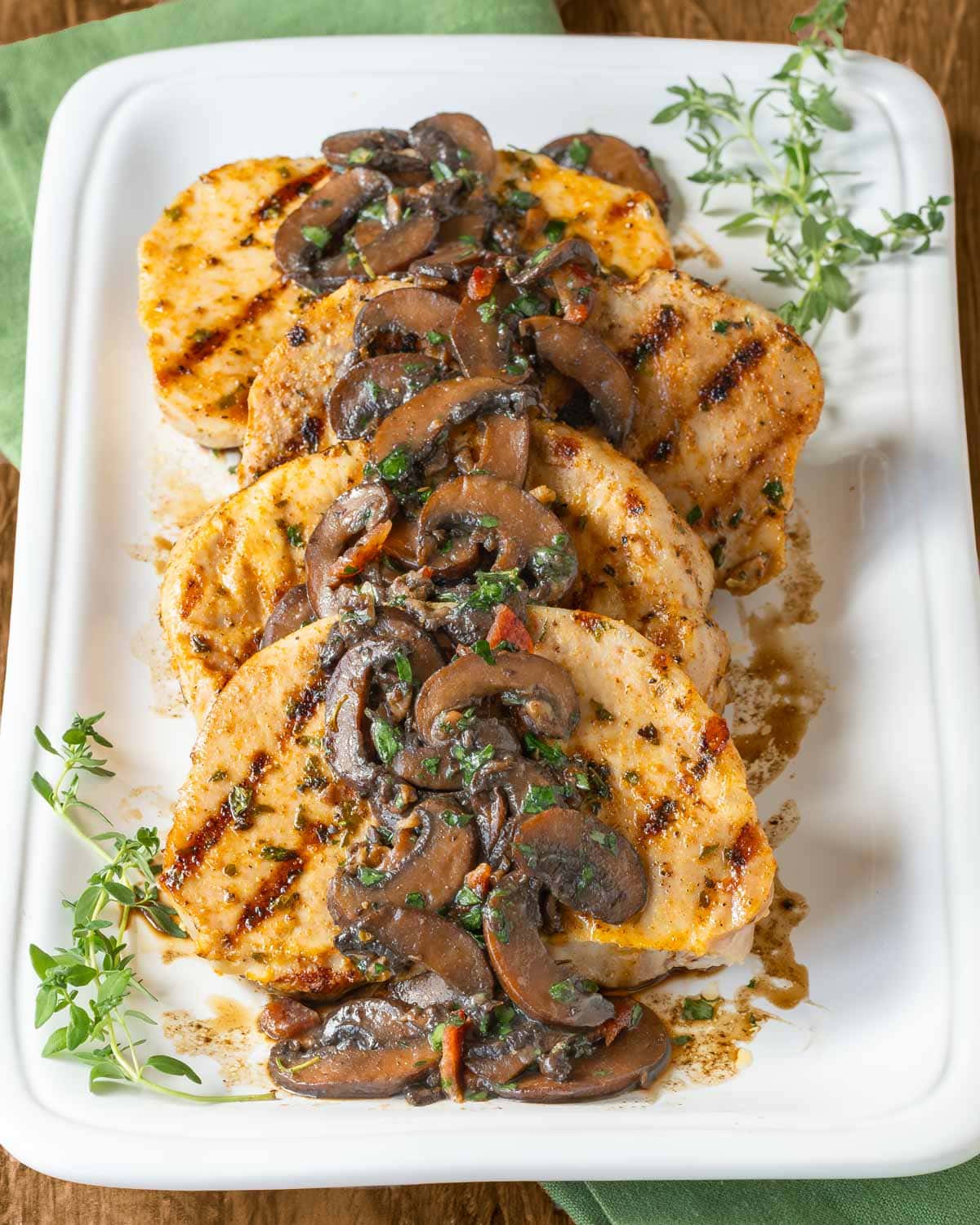 Four pork chops on a white latter with mushroom sauce spooned over top, garnished with fresh thyme