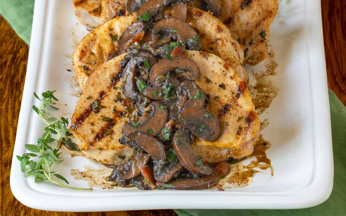 Close up of pork chops on a white latter with mushroom sauce spooned over top, garnished with fresh thyme