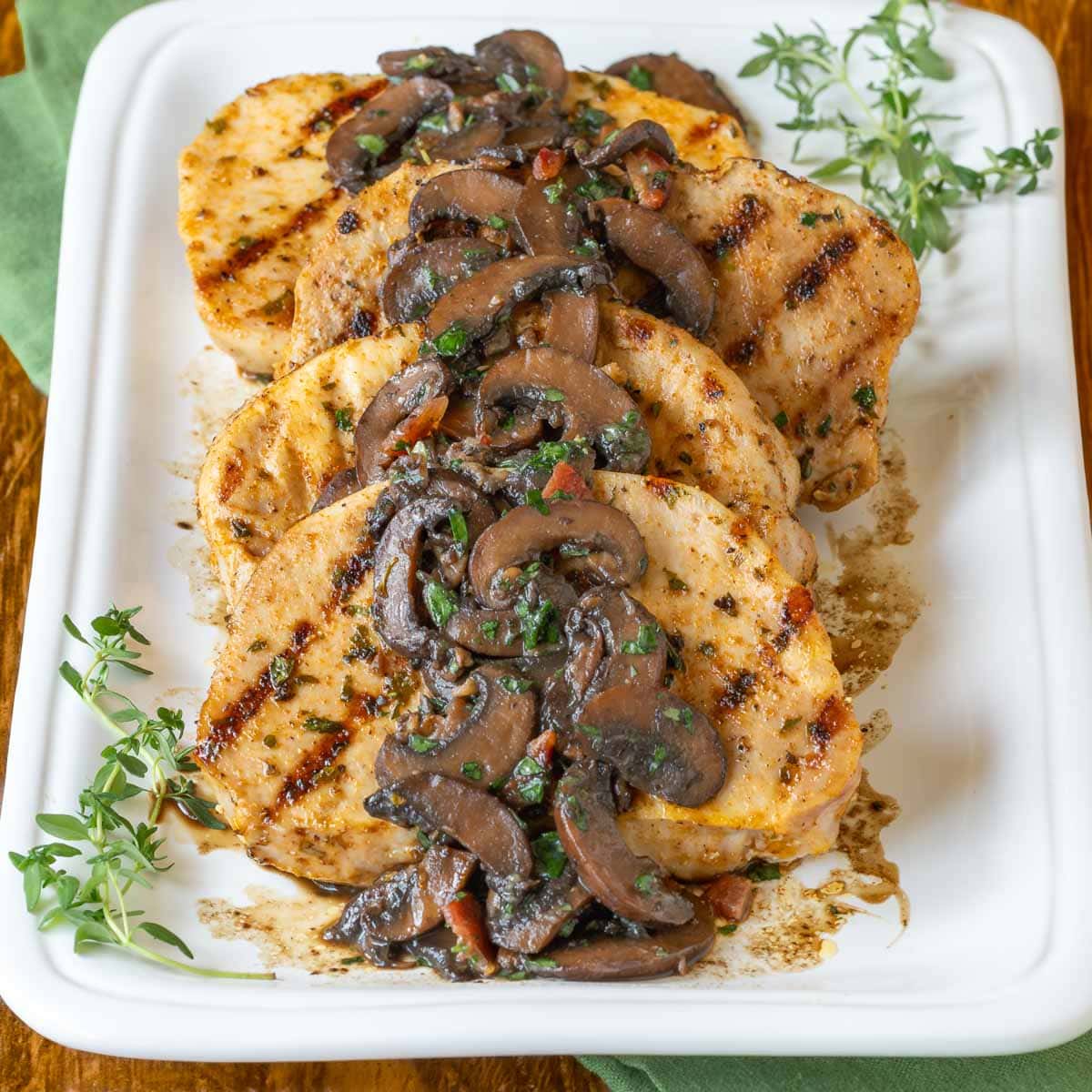 Four pork chops on a white latter with mushroom sauce spooned over top, garnished with fresh thyme