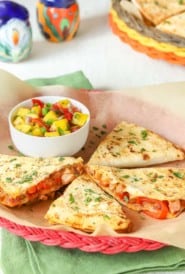 red wicker plate holding 4 slices (1 portion) of Leftover Pork Quesadillas with a small bowl of Tomato Mango Salsa alongside
