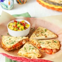 red wicker plate holding 4 slices (1 portion) of Leftover Pork Quesadillas with a small bowl of Tomato Mango Salsa alongside