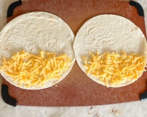 Overhead shot of two flour tortillas, open, with grated cheese on half of each