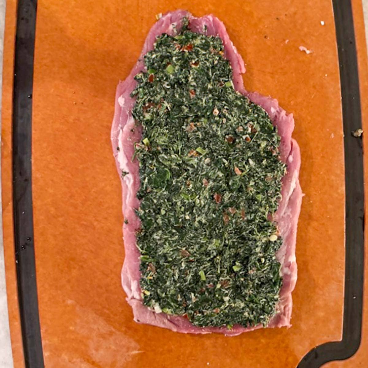 Spinach and cheese stuffing spread on butterflied raw pork tenderloin with ends cut off