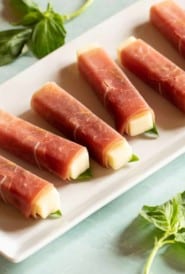 Narrow rectangular white platter filled with Prosciutto-Wrapped Smoked Mozzarella Sticks