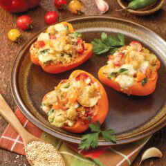 Three Stuffed Bell Peppers with Quinoa on a brown plate, with more ingredients surrounding the plate
