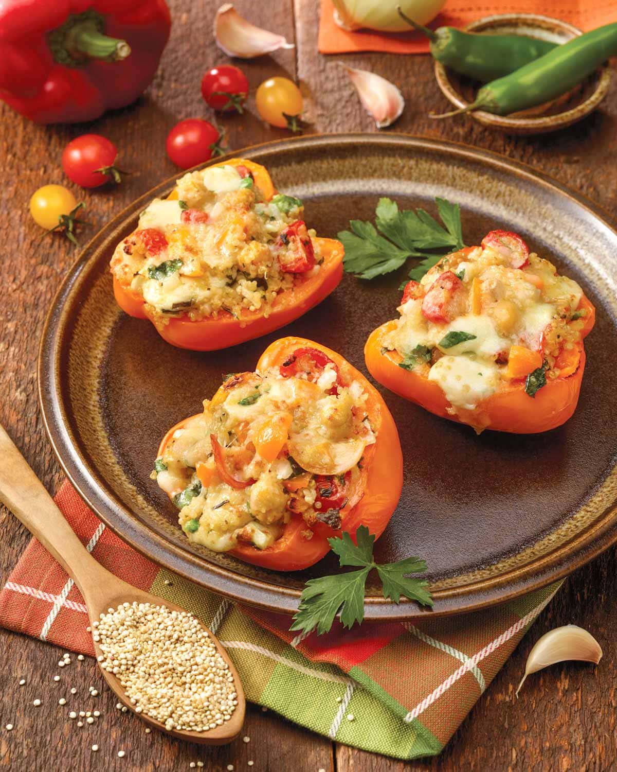 Three Stuffed Bell Peppers with Quinoa on a brown plate, with more ingredients surrounding the plate