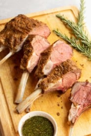 cutting board with sliced Mustard Crusted Rack of Lamb with Fresh Mint Sauce on the side