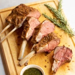 cutting board with sliced Mustard Crusted Rack of Lamb with Fresh Mint Sauce on the side