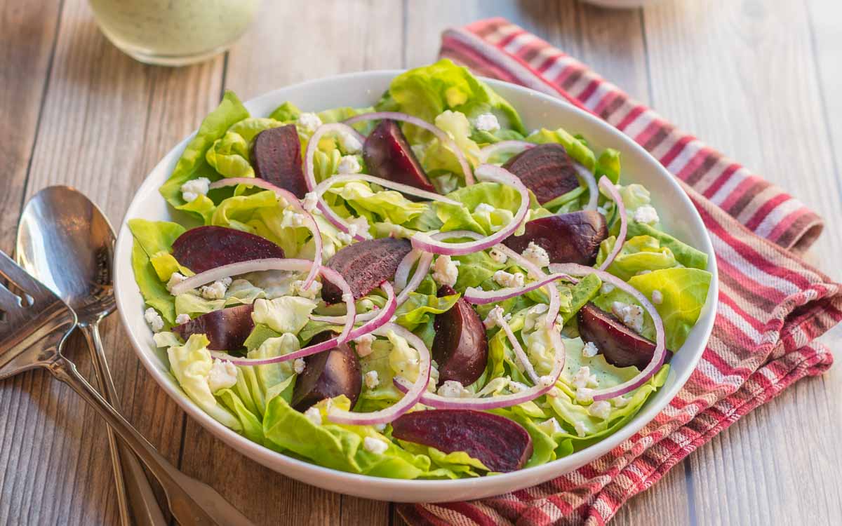 Closer look at a white bowl holding a portion of Roasted Beet Salad with Goat Cheese with Creamy Arugula Dressing on the side