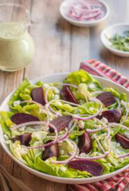 white bowl holding a portion of Roasted Beet Salad with Goat Cheese with Creamy Arugula Dressing on the side