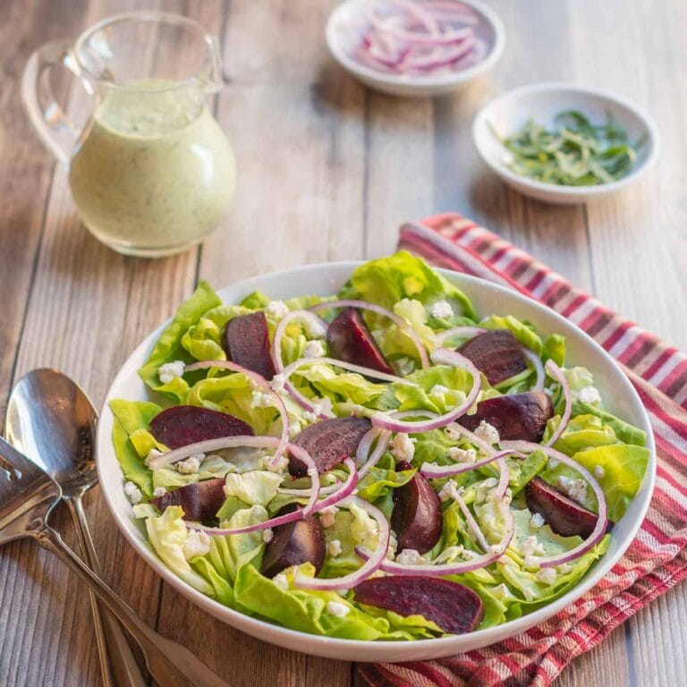 white bowl holding a portion of Roasted Beet Salad with Goat Cheese with Creamy Arugula Dressing on the side