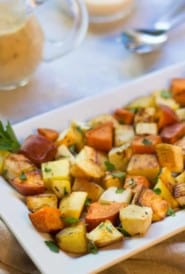 Retangular white platter filled with Roasted Root Vegetables, with a pitcher of mustard sauce on the side