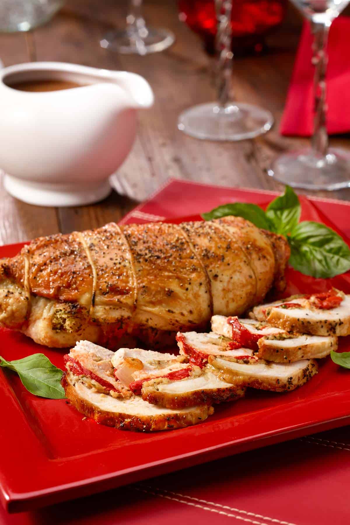 Red plate with sliced and whole Rolled Turkey Breast with Roasted Red Pepper Stuffing