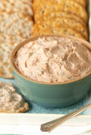 Close up shot of Smoked Salmon Mousse in a blue bowl, with a cracker with mousse on it to the side and more crackers in the back