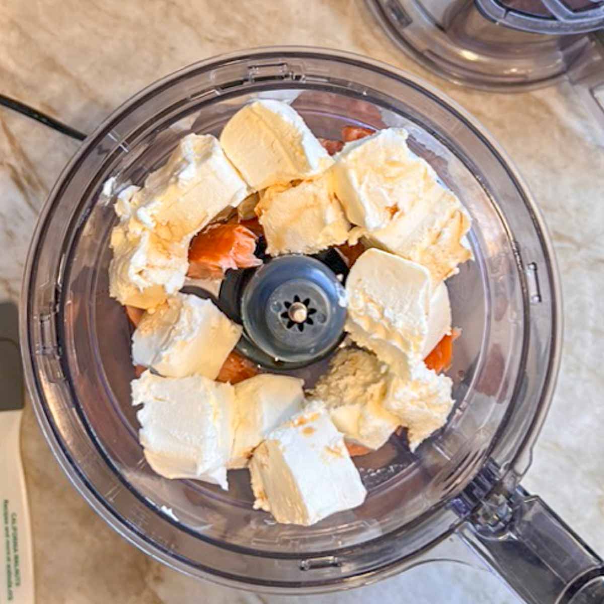 overhead shot of cubed cream cheese and chopped salmon in food processor