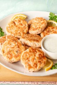 round plate holding several salmon patties, along with a bowl of Tzatziki sauce on the side.