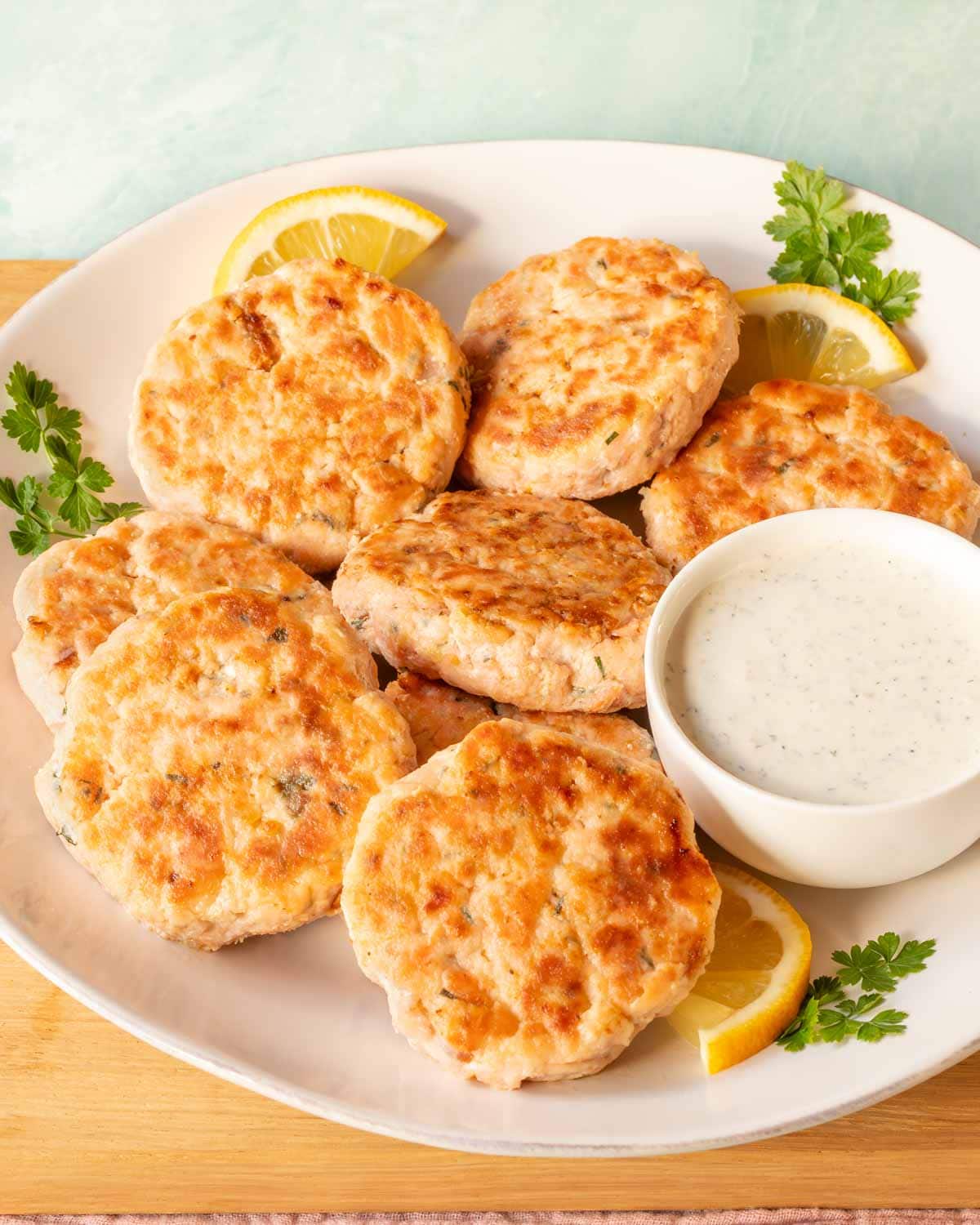 round plate holding several salmon patties, along with a bowl of Tzatziki sauce on the side