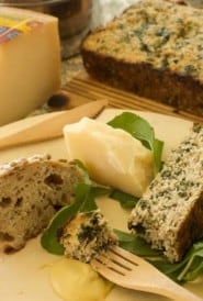 Wooden plate with sliced Sausage and Spinach Torte, alongside a wedge of cheese