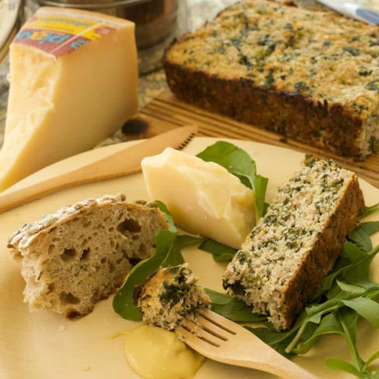 Wooden plate with sliced Sausage and Spinach Torte, alongside a wedge of cheese