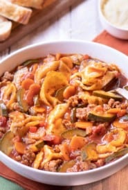 Bowl of soup with tortelloni, sausage, zucchini and carrots.