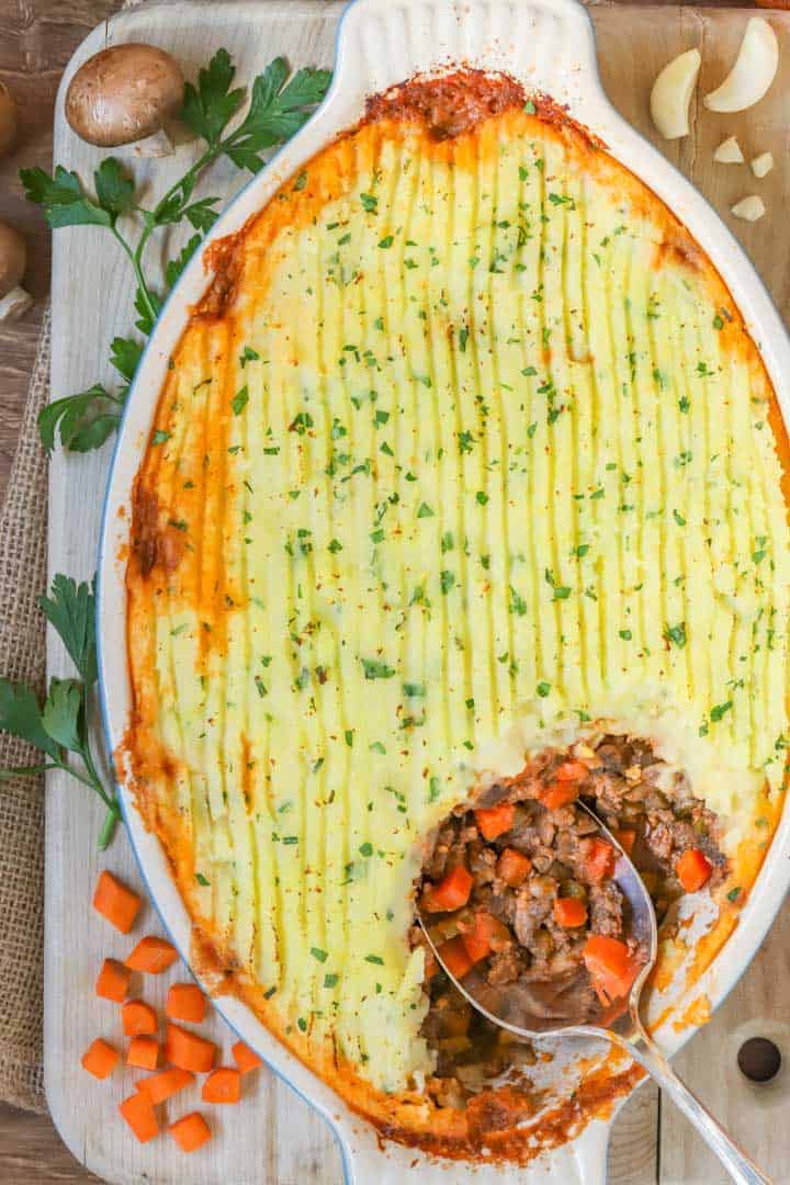 overhead view of an oval baking dish filled with Shepherd's PIe, with one corner scooped out showing the filling