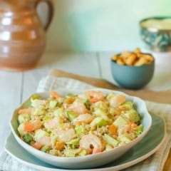 Chopped Shrimp Salad with Rice and Avocado mounded on top of a blue plate, with cashews and a pitcher if flowers in the background