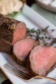whole roasted beef tenderloin with a few slices in front and sauce on the side