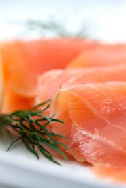 rolled pieces of smoked salmon on a white platter with dill and a lemon slice