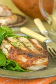 One Sous Vide Pork Chop on a silver plate with a side of arugula, with more chops in the background