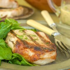 One Sous Vide Pork Chop on a silver plate with a side of arugula, with more chops in the background