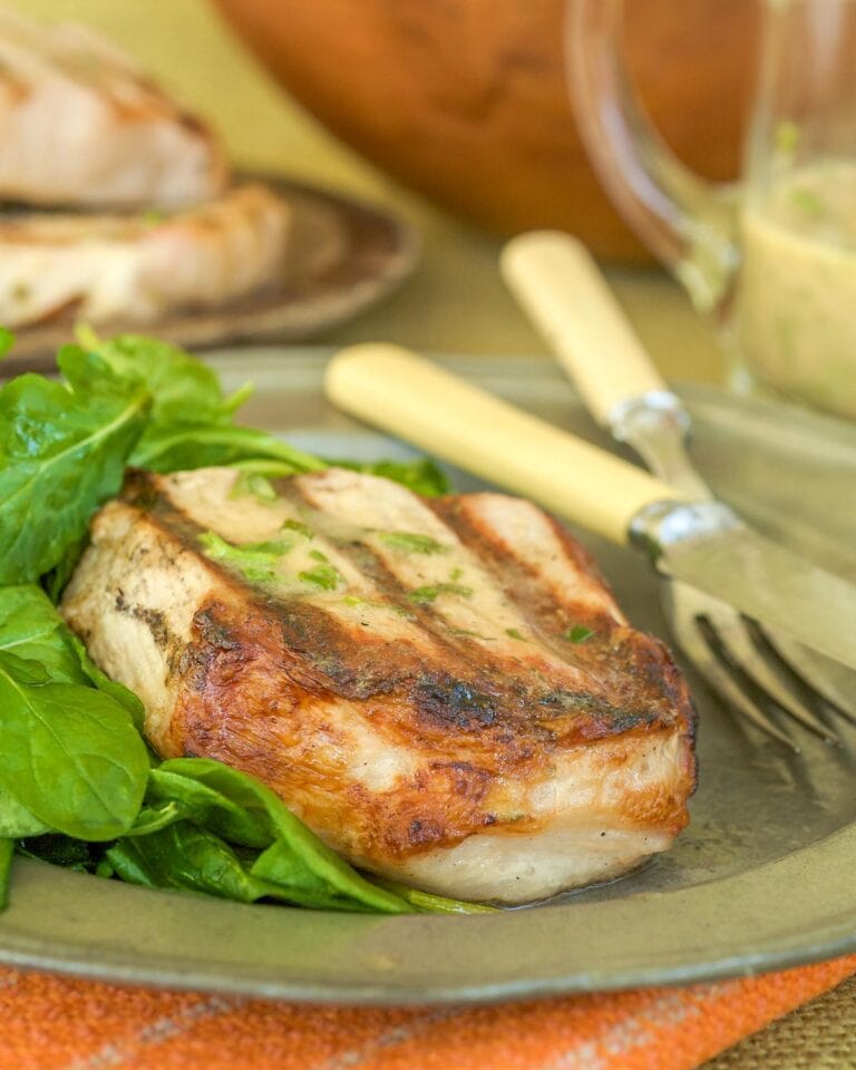One Sous Vide Pork Chop on a silver plate with a side of arugula, with more chops in the background