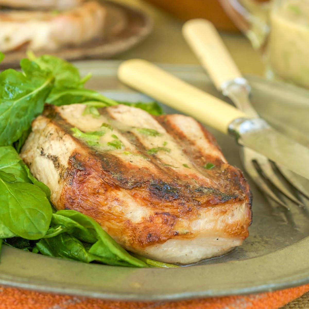 One Sous Vide Pork Chop on a silver plate with a side of arugula, with more chops in the background