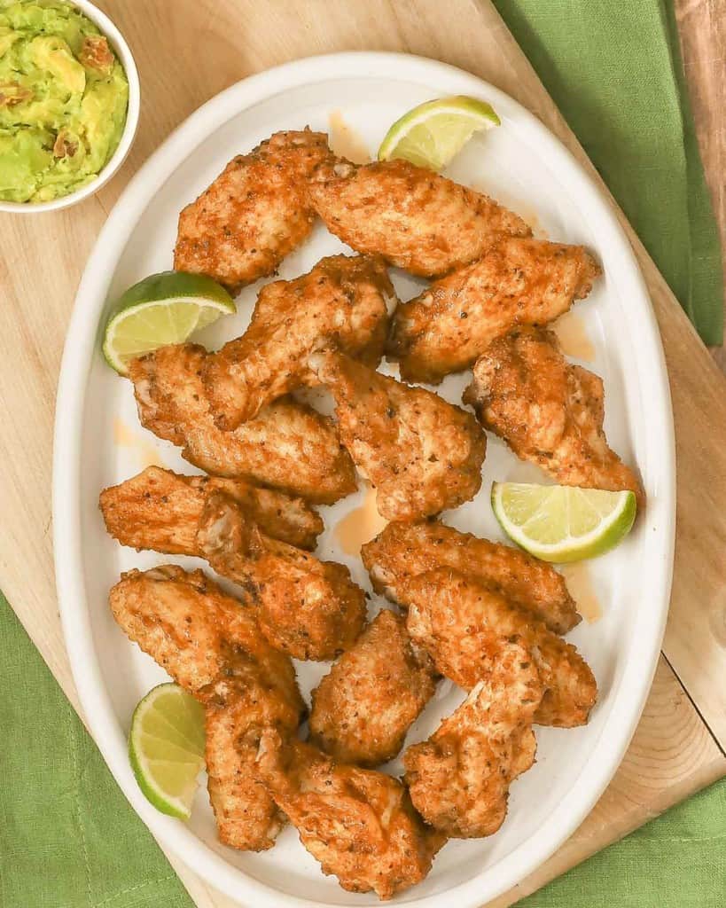 overhead shot of a large oval white platter filled with spicy chicken wings; guacamole in a bowl on the side