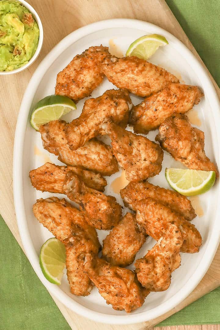 overhead shot of a large oval white platter filled with spicy chicken wings; guacamole in a bowl on the side
