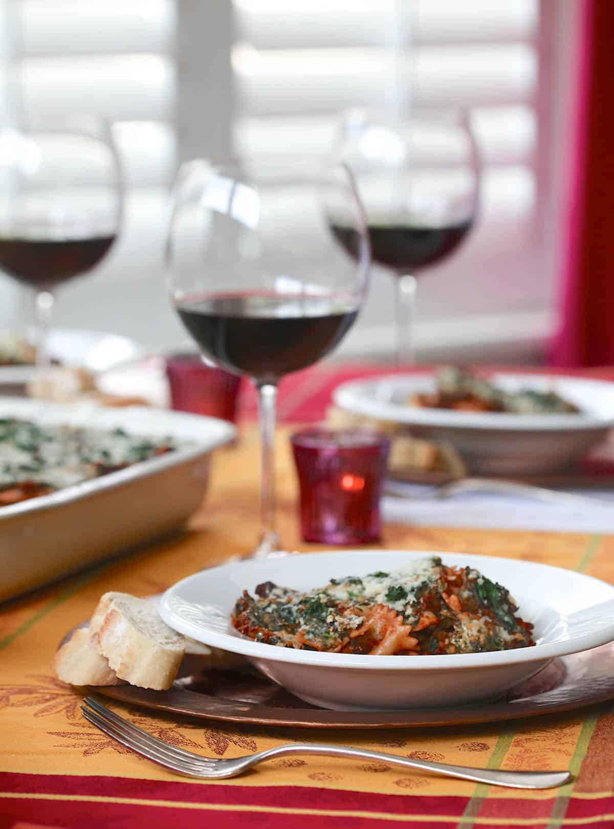 table set with plates of Spinach Farfalle Bolognese and glasses of red wine