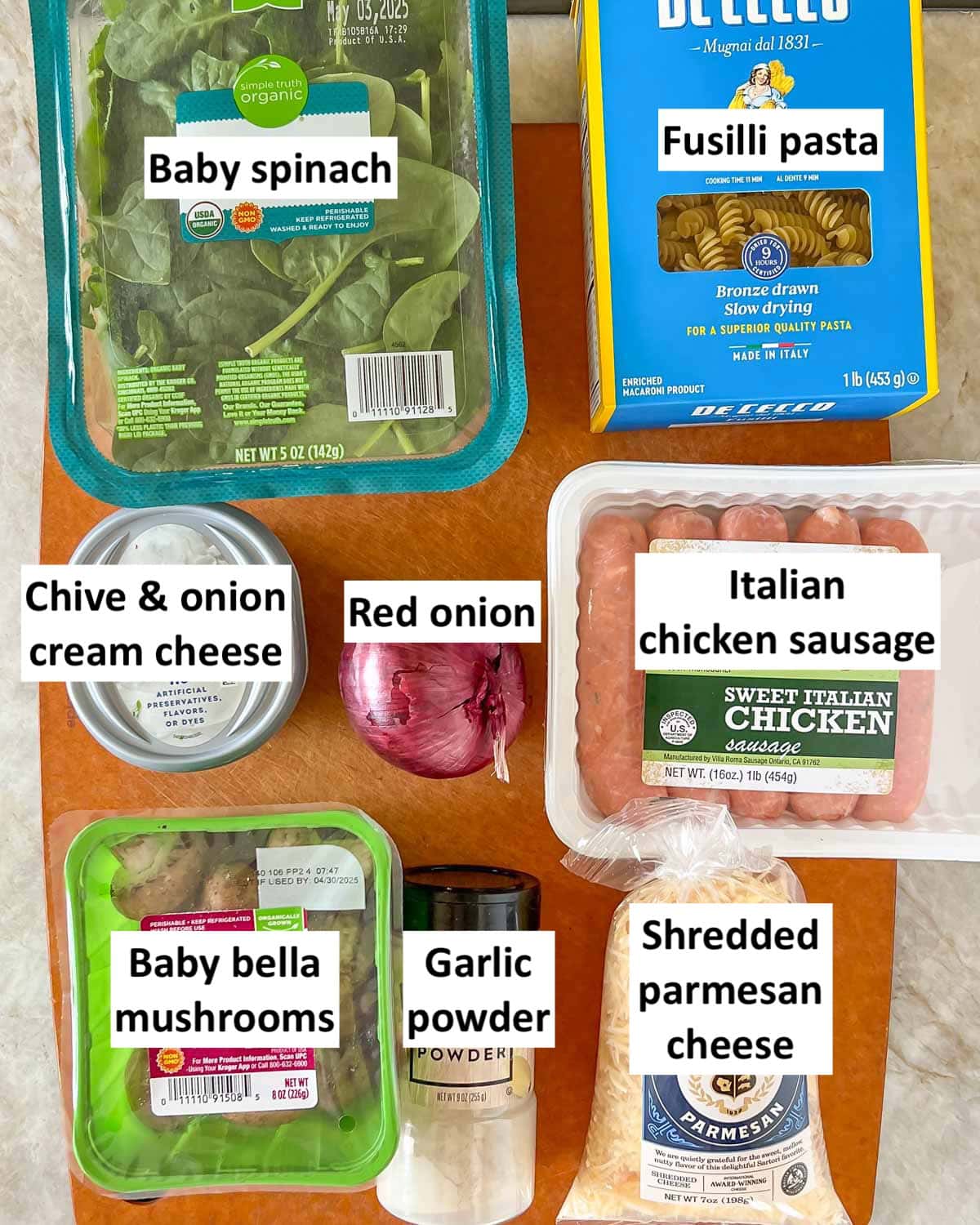 cutting board holding all of the ingredients in sausage, spiach and mushroom pasta, with each one labeled