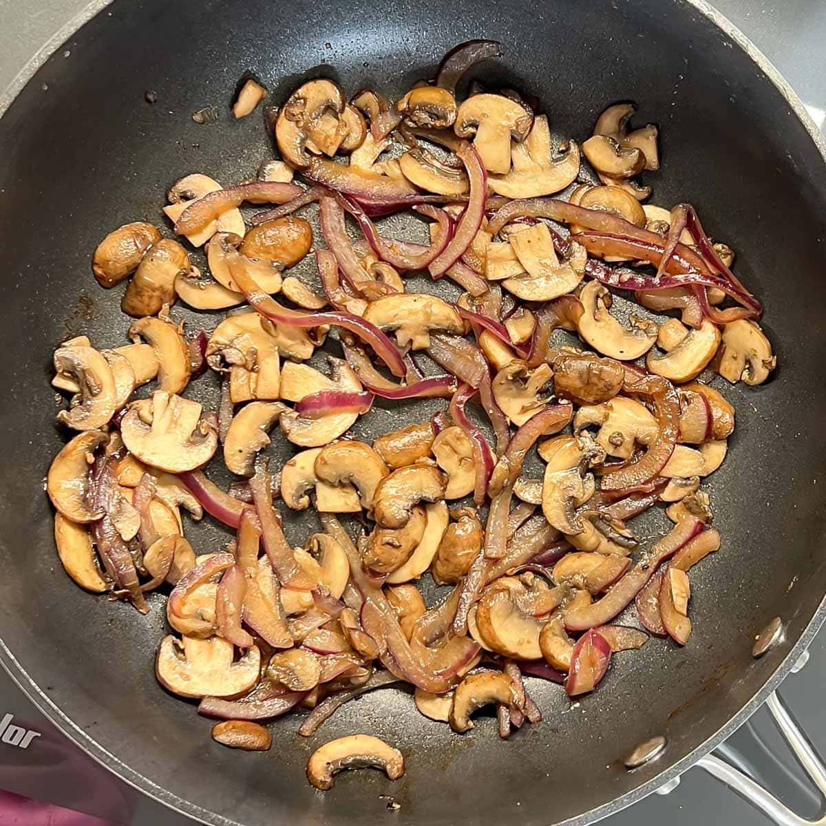 sliced mushrooms and read onion cooking in a black sauté pan