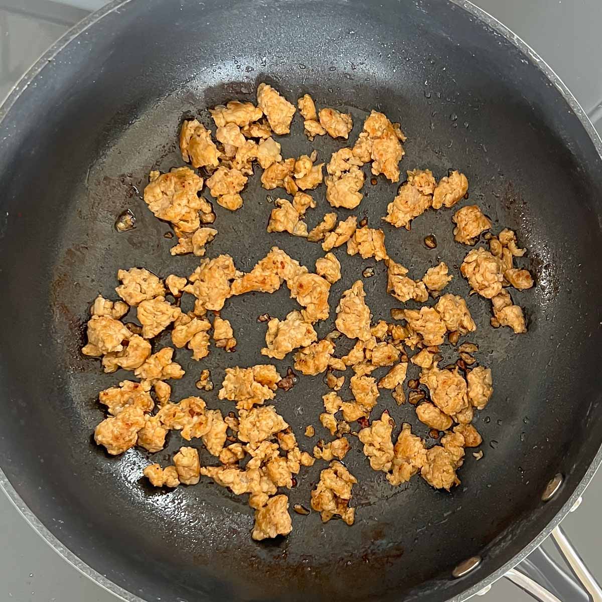 chicken sausage browning in a black sauté pan; chicken has been broken into 1/2 inch pieces