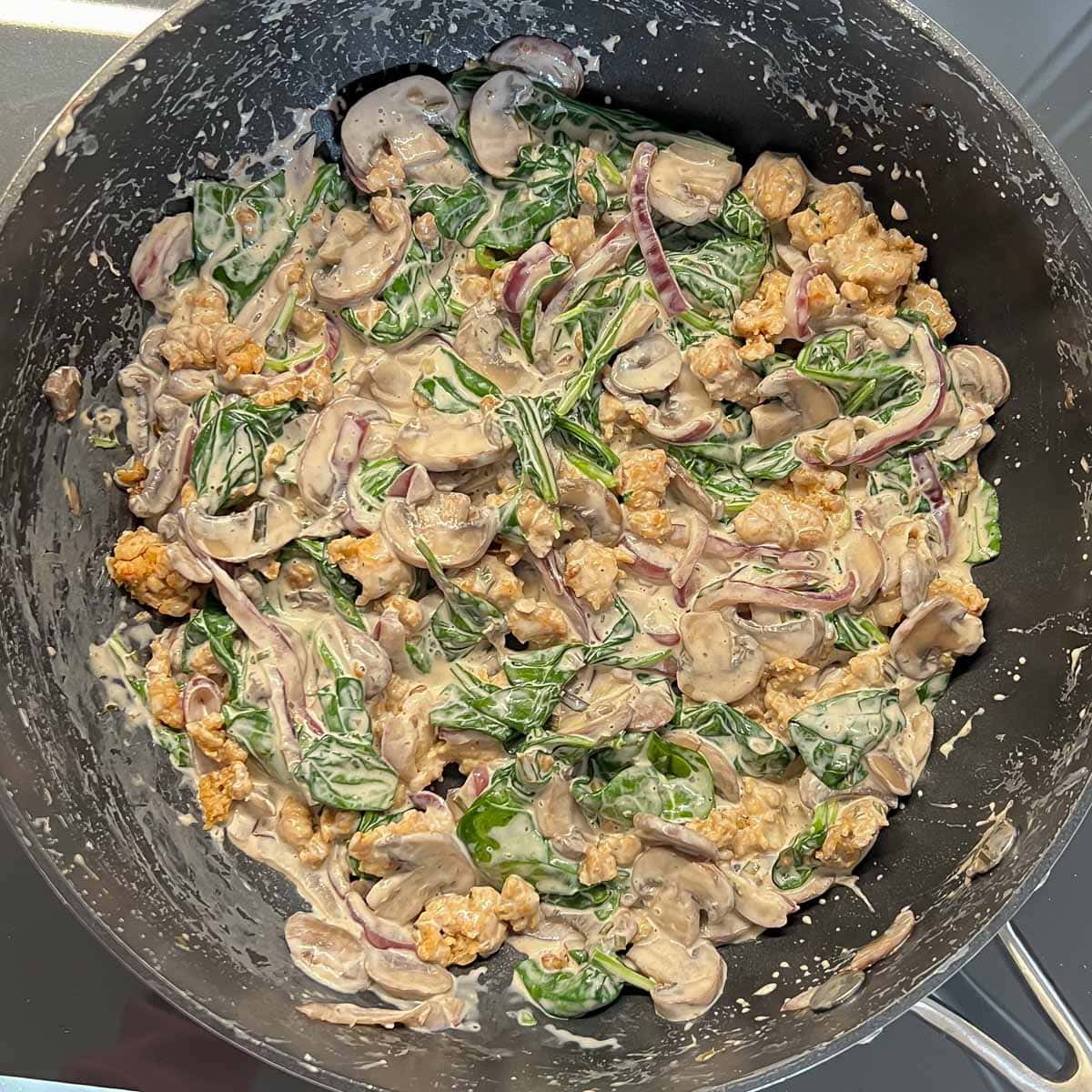 browned chicken sausage, cooked mushrooms and onions, baby spinach, cream cheese and Parmesan cheese all mixed together in a black sauté pan