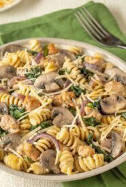 Closer view of a bowl holding a large portion of chicken sausage, spinach, and mushroom pasta, with grated Parmesan