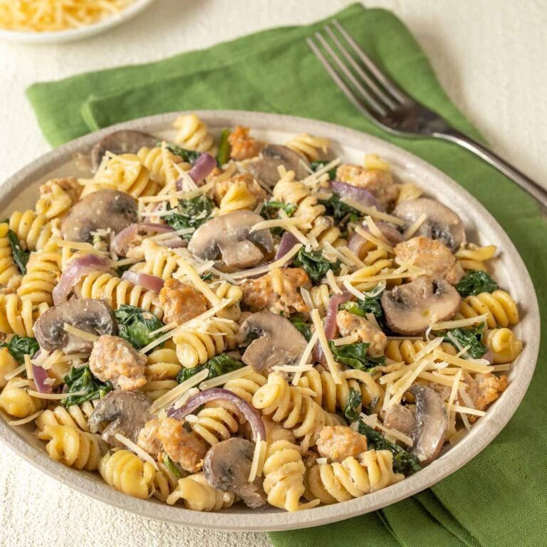 Closer view of a bowl holding a large portion of chicken sausage, spinach, and mushroom pasta, with grated Parmesan