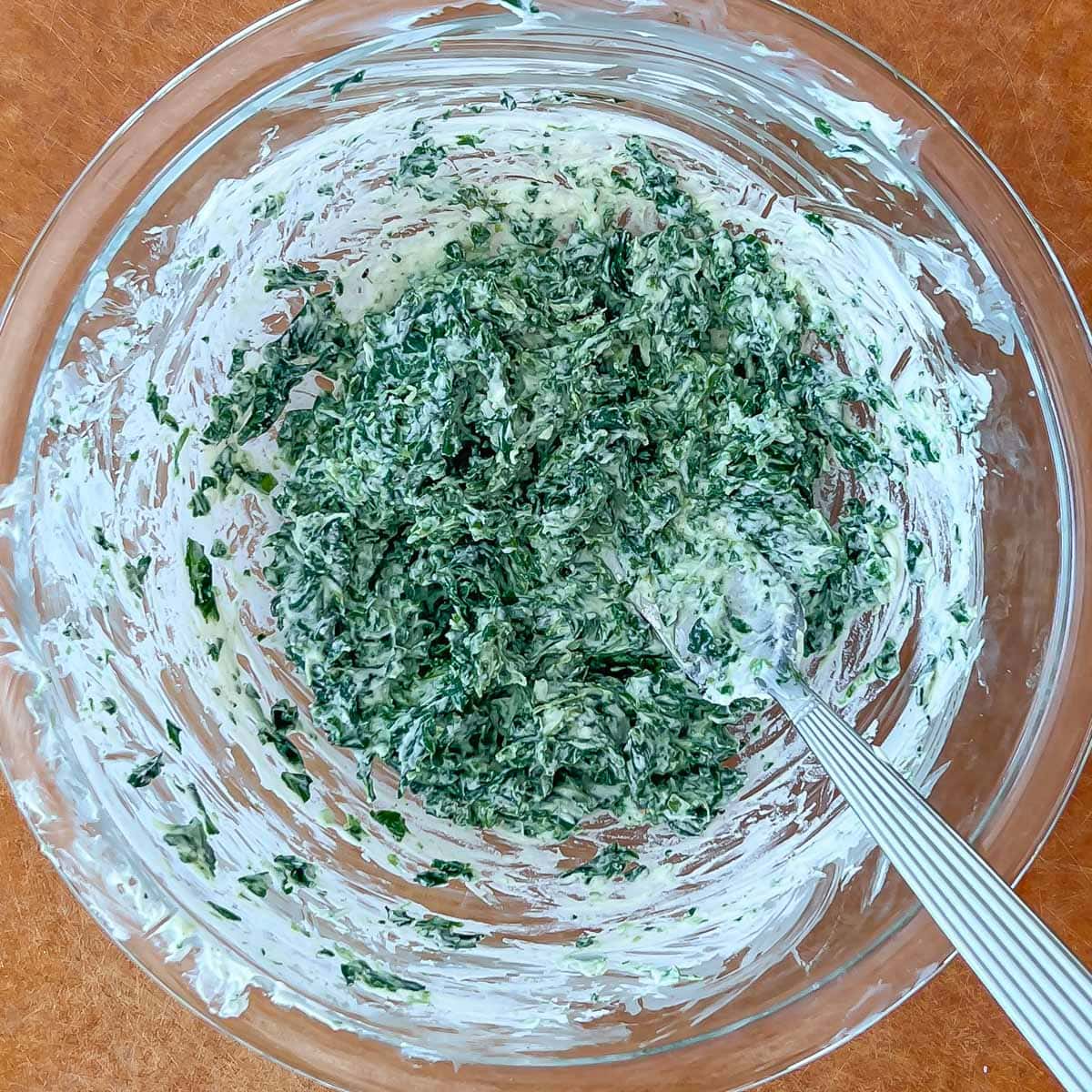 Process shot of spinach, mascarpone, cream cheese, and nutmeg mixed with a fork