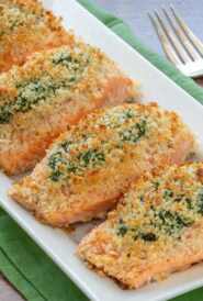 White serving platter holding 4 servings of Spinach Stuffed Salmon, with a serving fork alongside and plates in the background